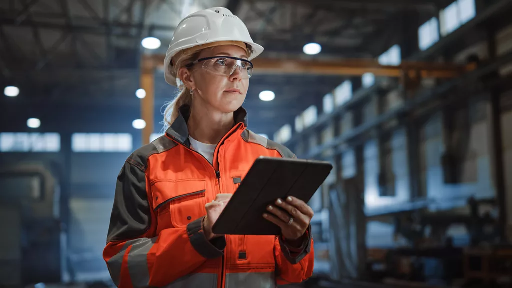 Woman in hard hat with clipboard in factory.