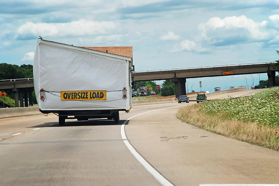 Section of manufactured home being hauled on a freeway with "oversize load" sign on the back. 