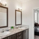 primary bath with double sink vanity and dual mirrors with tile backsplash, dark wood cabinets, and nickel hardware