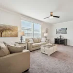 spacious living room with central ceiling fan, two windows, and hallway leading to the bedrooms