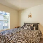 queen bed in an empty bedroom with plush carpeting and large window