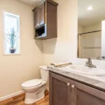 single sink bathroom vanity beside porcelain toilet with mounted wall cabinet across from a traditional tub shower