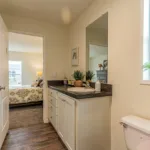 single sink vanity with dark grey counters, nickel hardware, and white cabinets next to a toilet