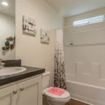 single sink vanity with dark grey counters, nickel hardware, and white cabinets next to a toilet and traditional tub shower