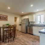 dining nook opposite an open kitchen with dark granite counters, stainless steel appliances, white cabinets, and nickel hardware