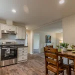 dining nook opposite an open kitchen with dark granite counters, stainless steel appliances, white cabinets, and nickel hardware