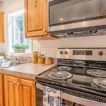 corner kitchen with stainless steel appliances, warm grey counters, dual sinks, rich wood cabinets, and nickel hardware