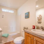 single sink vanity with grey granite counters, rich wood cabinets, and nickel hardware next to a traditional tub shower