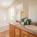 dual sink vanity with grey granite counters, rich wood cabinets, and nickel hardware next to a traditional tub shower