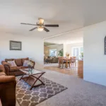 living room with brown suede sofa and loveseat and glass-top coffee table leading into a kitchen