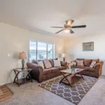 living room with brown suede sofa and loveseat and glass-top coffee table leading into a kitchen