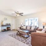 living room with brown suede sofa and loveseat and glass-top coffee table leading into a kitchen