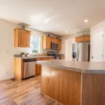 corner kitchen with stainless steel appliances, warm grey counters, dual sinks, rich wood cabinets, and nickel hardware