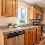 corner kitchen with stainless steel appliances, warm grey counters, dual sinks, rich wood cabinets, and nickel hardware