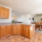 corner kitchen with warm grey granite counters and rich wood cabinets with nickel hardware looking out over an attached dining door and living room